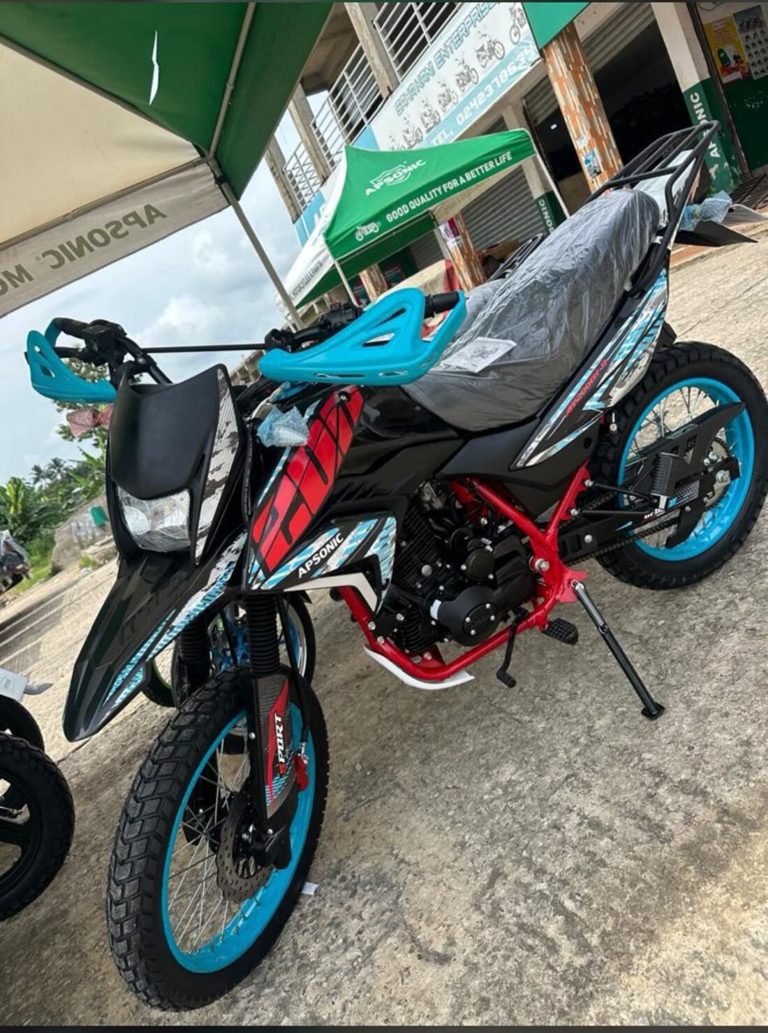 A new Apsonic trail bike, still in its plastic, parked under the green Apsonic canopy outside the shop